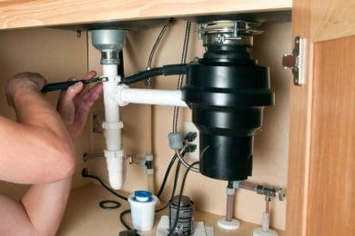 Plumber repairing a garbage disposal beneath a kitchen sink in Cartersville