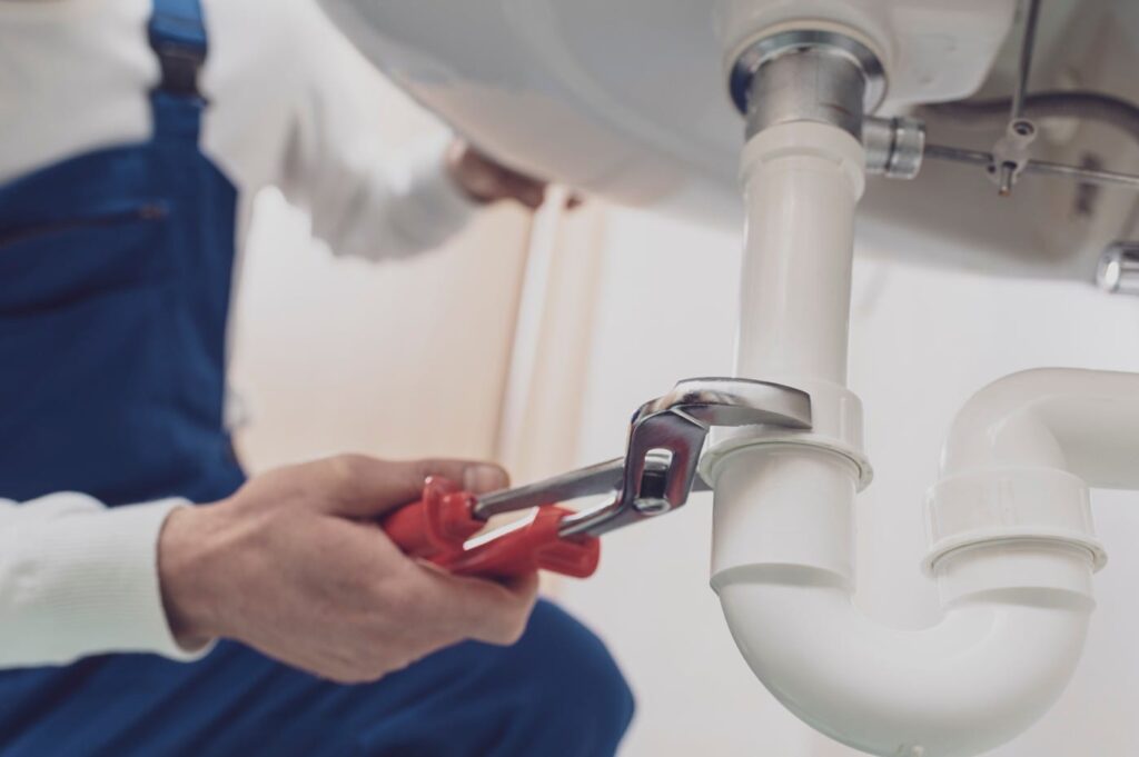 Plumber repairing a white drain pipe beneath a sink in Cartersville